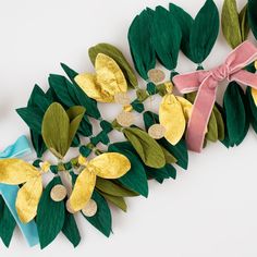 paper flowers and green leaves are arranged on a white surface with pink ribbon tied around them