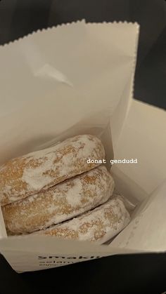 three powdered donuts in a white paper bag