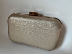 "This Jessica Simpson brand case is covered in light gold-color textured vinyl over the hard shell and is roomy enough for your evening essentials. The bag has a bright gold-color frame, rectangular tip-up clasp, and hinges. The interior is lined in champagne or ivory fabric. Including the clasp, the bag is 4 1/4\" high x 6 1/2\" wide x 1 7/8\" thick. To open, tip up the lower edge of the clasp. One slight blemish on back (pictured)." Elegant Metallic Rectangular Evening Bag, Metallic Rectangular Clutch For Formal Events, Metallic Rectangular Clutch For Formal Occasions, Classic Gold Clutch With Gold-tone Hardware, Gold Rectangular Case Clutch For Formal Occasions, Gold Rectangular Clutch For Formal Occasions, Gold Rectangular Case Evening Bag For Formal Occasions, Chic Gold Evening Bag With Rectangular Case, Classic Gold Rectangular Clutch