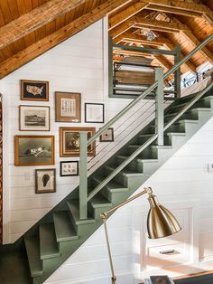 a room with stairs and pictures on the wall next to a desk in front of a lamp