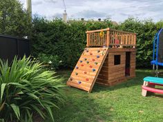 there is a small wooden play set in the yard with a slide and climbing wall