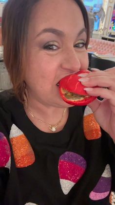 a woman is eating something with her mouth open and wearing an orange, pink, and purple sweater