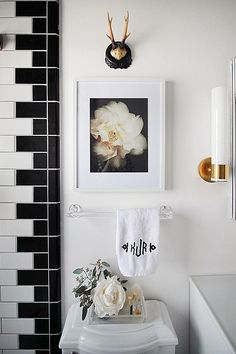 a bathroom with black and white tiles, gold faucet, framed pictures and flowers on the wall