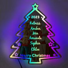 a lighted christmas tree ornament with the names of three people standing in front of it