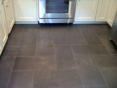 a kitchen with white cabinets and gray tile flooring, stainless steel oven and dishwasher