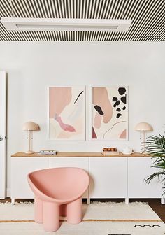 a living room with two paintings on the wall and a pink chair in front of it