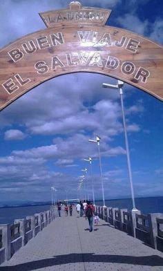 people walking on a bridge over the ocean under a blue sky with white fluffy clouds