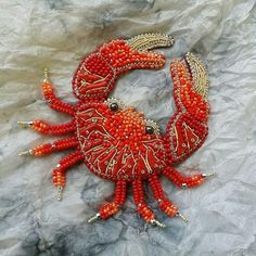 a red crab brooch sitting on top of a white piece of paper with beads