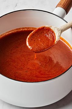 a wooden spoon full of tomato sauce in a white bowl