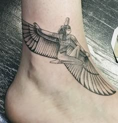 a black and white tattoo on the foot of a woman with an egyptian winged bird