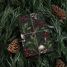 a present wrapped in wrapping paper on top of pine cones and evergreen branches with skulls