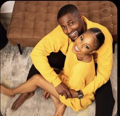 a man and woman are sitting on the floor in front of a couch smiling at the camera