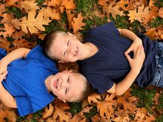 two young boys laying on top of leaves in the grass with their arms around each other