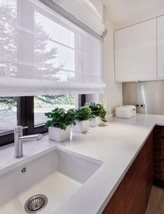 a kitchen with white counter tops and wooden cabinets next to a window that has blind shades on it