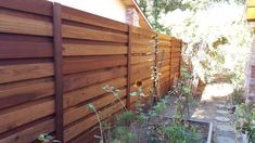 a wooden fence next to a house with flowers growing in the yard and on the side