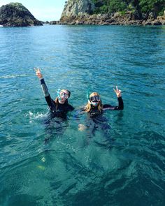 two people wearing scuba gear in the water with their hands up and one person holding her hand up