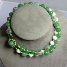 Here's a vintage green art glass bead choker necklace from the mid century.  It features an assortment of jade green glass beads, some of which have embedded color swirls.  Beads are all in nice condition, and necklace measures 14" long with a decorative box clasp.  Can easily be made into a single long strand.  Matching clip earrings will be included, but they are not in good condition.  Please see the image with the coin for a size comparison as images often appear larger than actual size. This is necessary to provide accurate details.   Thanks for looking. Green Glass Round Bead Jewelry, Vintage Green Glass Beaded Necklaces, Green Vintage Glass Beaded Necklaces, Adjustable Vintage Jade Necklace, Vintage Adjustable Jade Necklace, Adjustable Vintage Jade Necklaces, Vintage Adjustable Jade Necklaces, Vintage Jade Beaded Necklaces, Vintage Green Round Beads Jewelry