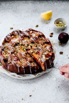 someone cutting into a cake on top of a white plate with icing and nuts