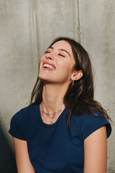 a woman smiling and looking up with her eyes closed while wearing a blue shirt against a concrete wall