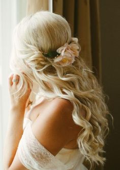 a woman with long blonde hair wearing a flower in her hair, looking out the window