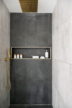 a walk in shower sitting next to a tiled wall with shelves on each side and gold fixtures