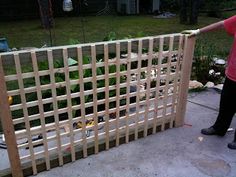 a man standing next to a wooden trellis on top of a cement floor in front of a yard