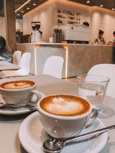 two cups of cappuccino sitting on top of a white table next to each other