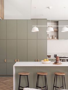 three stools sit at the bar in this modern kitchen with green cabinets and white countertops