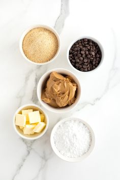 four bowls filled with different types of food on top of a marble countertop next to chocolate chips and butter