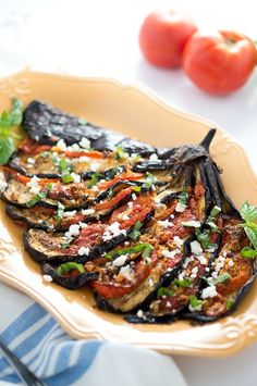 grilled eggplant with tomatoes and feta cheese on a yellow platter