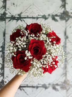 a bouquet of red roses and baby's breath is being held by a hand