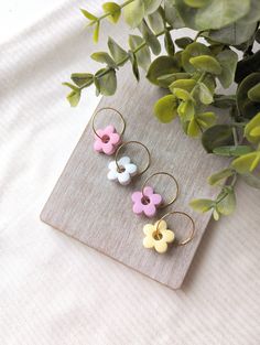 three flower shaped earrings sitting on top of a wooden board next to a potted plant