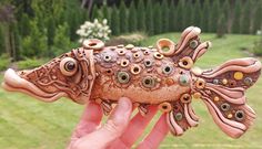 a hand holding a clay fish sculpture in the shape of a fish with eyes on it's body