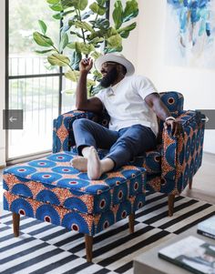 a man sitting on a blue couch in front of a window with a plant growing out of it