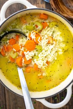 a pot filled with rice and carrots on top of a wooden table next to a spoon