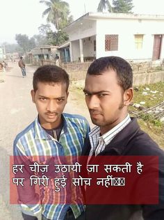 two men standing next to each other on a road near some houses and trees in the background