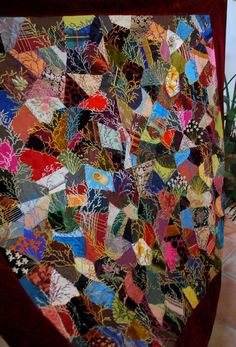 a very colorful quilt hanging on the side of a wall next to a potted plant