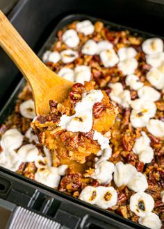 a wooden spoon scooping some food out of a casserole dish with marshmallows