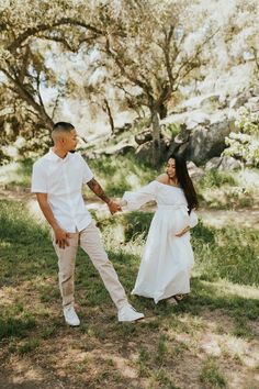 a man and woman holding hands while standing in the grass with trees in the background