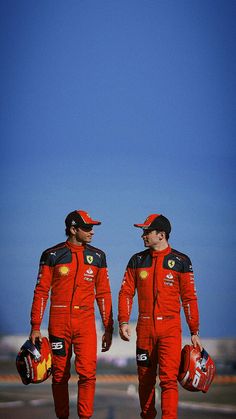 two men in red racing suits walking on the tarmac