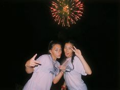 two young women standing next to each other in front of a firework display at night