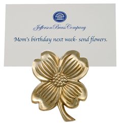 a gold flower brooch sitting on top of a white card with the words mom's birthday next week - send flowers