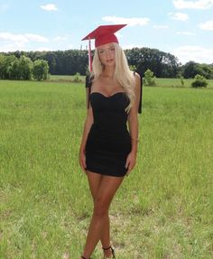 a woman in a black dress and red graduation cap poses for a photo on the grass