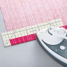 ironing board next to pink and white fabric on grey surface with ruler in foreground