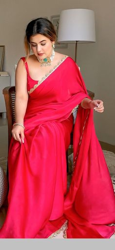 a woman in a red sari is sitting on a chair and looking down at the floor