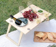 a picnic table with wine, grapes and bread on it next to a bottle of wine