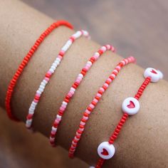 four bracelets with red and white beads on a woman's arm, one has a heart