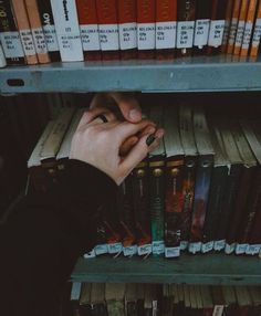 a person's hand on top of a book shelf in front of many books