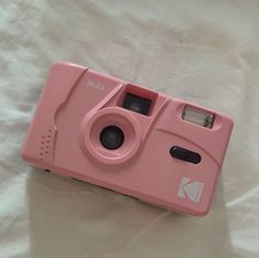 a pink camera sitting on top of a white sheet