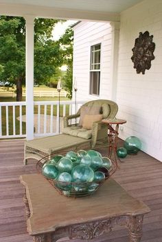 a bowl of green glass balls sitting on top of a wooden table in front of a white house